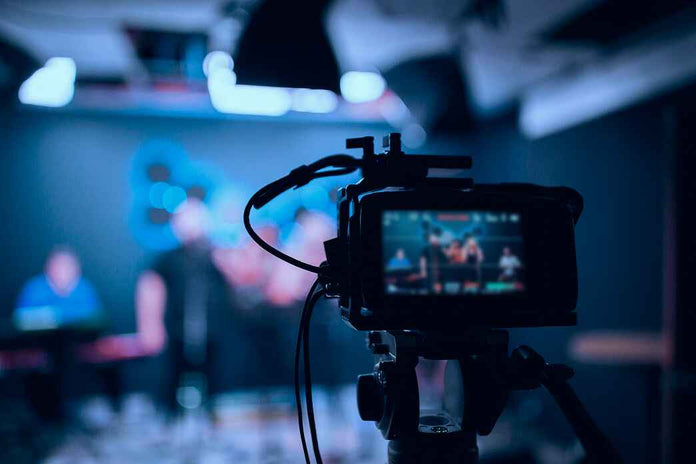Camera on a tripod recording a blurred indoor setting with people.