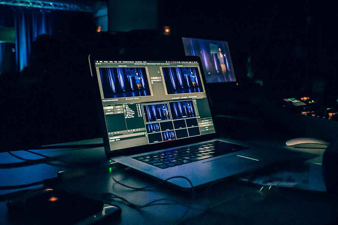 Laptop on a dark desk with multiple screens displaying video editing software.